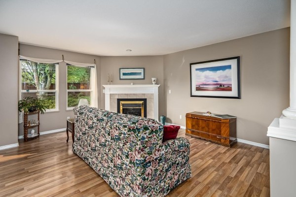 Living room with fireplace, floral sofa, wood floors, and large windows. - 252 13888 70 Avenue, Surrey