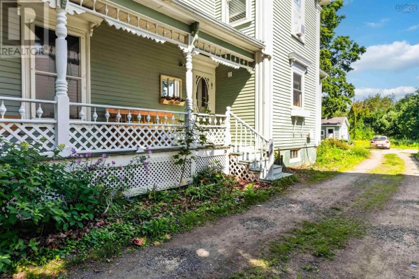 Close-up of the porch detailing, showing white lattice work, decorative trim, and a gravel driveway. - 252 Main Street, Berwick
