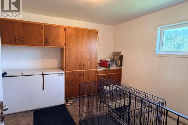 Interior view of a room with a white chest freezer, wooden cabinets, and a dog crate. - 252 Railway Avenue, Forget