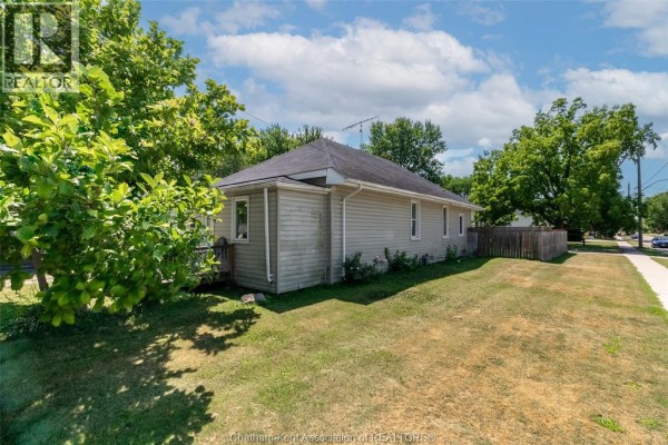Side view of the bungalow showing light grey siding and a grassy lawn. - 252 Wellington Street East, Chatham