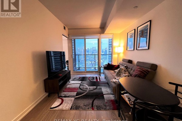 Living area with grey sofa, tv, dining table, and balcony view. - 2520 - 19 Western Battery Road, Toronto