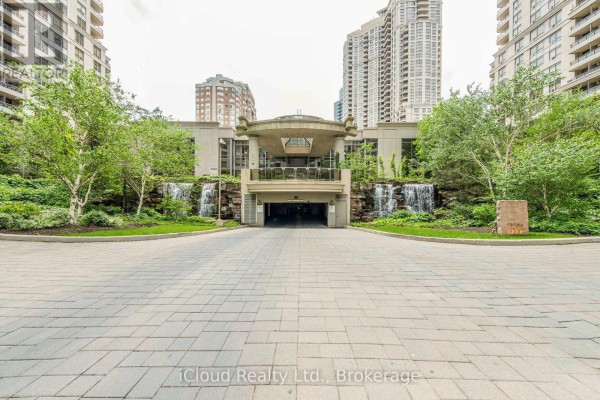 Apartment building entrance with covered driveway, waterfalls, and surrounding greenery. - 2521 - 3888 Duke Of York Boulevard, Mississauga