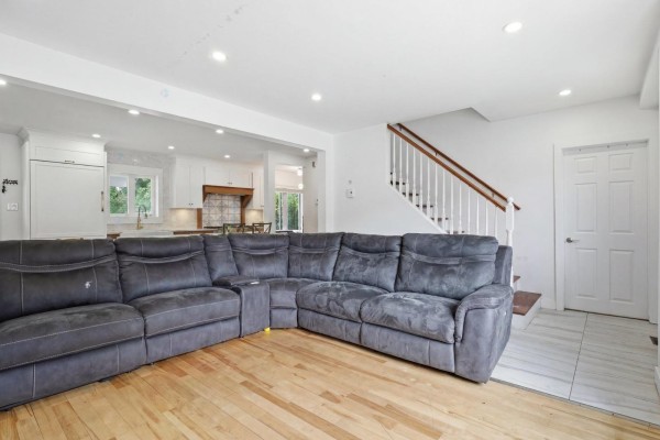 Living area with a large sectional sofa, hardwood floors, and a view of the staircase and kitchen. - 2523 Rue St-louis, Gatineau