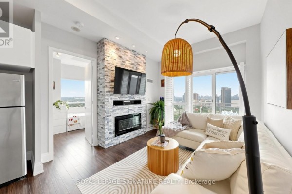Living room with fireplace, white sectional sofa, floor lamp, and large windows. - 2524 - 165 Legion Road, Toronto
