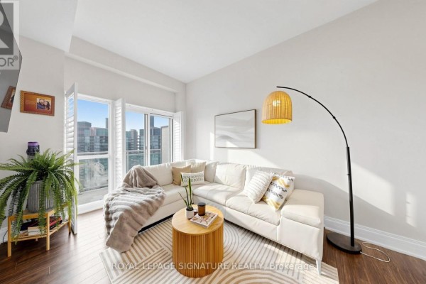 Living room with corner sectional sofa, coffee table, floor lamp, and city view. - 2524 - 165 Legion Road, Toronto