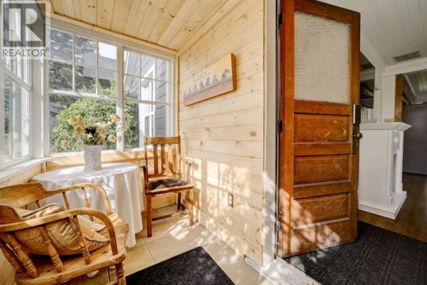 Sunroom with wood paneling, two chairs, a small table, and large windows. - 2526 211 Street, Bellevue