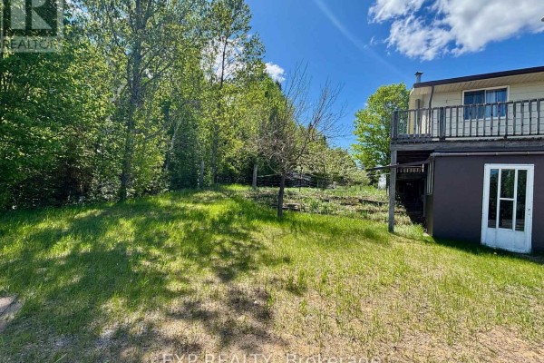 Grassy yard with scattered trees leading up to the side of the house. - 2527 Matawatchan Road, Greater Madawaska