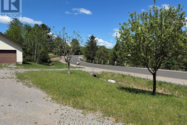View of the road curving through a treed landscape with the garage on the left. - 2527 Matawatchan Road, Greater Madawaska