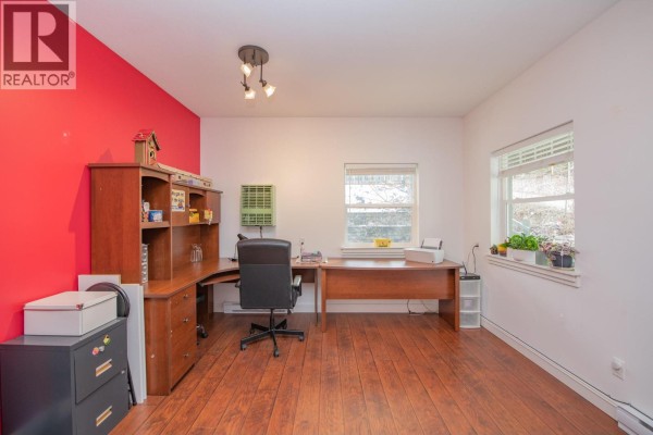 Home office with red accent wall, wooden desk, and large window for natural light. - 2529 Cedar Ridge Court, Lumby