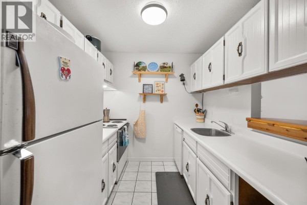 Galley kitchen with white cabinets, a white refrigerator, and tiled flooring. - 253 5421 10th Avenue, Delta