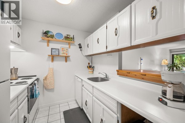Another view of the galley kitchen with white counters and upper cabinets. - 253 5421 10th Avenue, Delta