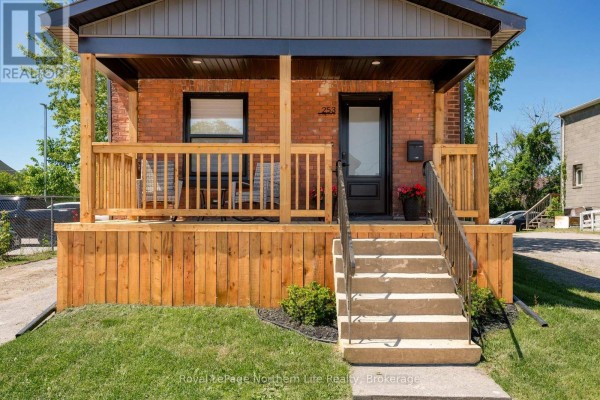 Close-up of the wooden porch and front entrance of a brick building, with a rocking chair and potted plants. - 253 Second Avenue W, North Bay