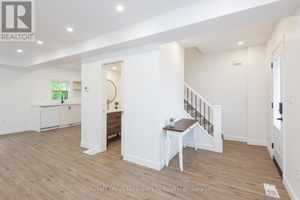 Open concept interior showing a living area, a small bathroom vanity, and stairs leading up. - 253 Second Avenue W, North Bay