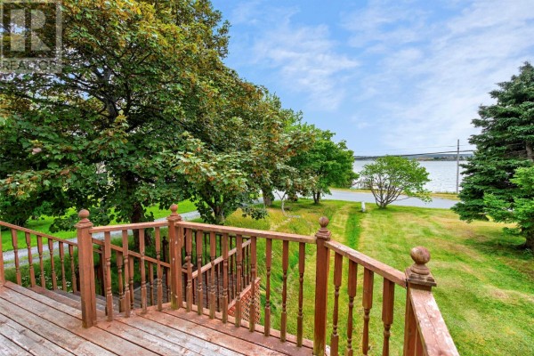 Wooden deck railing overlooking a grassy yard and a distant body of water under a blue sky. - 253 Water Street, Bay Roberts