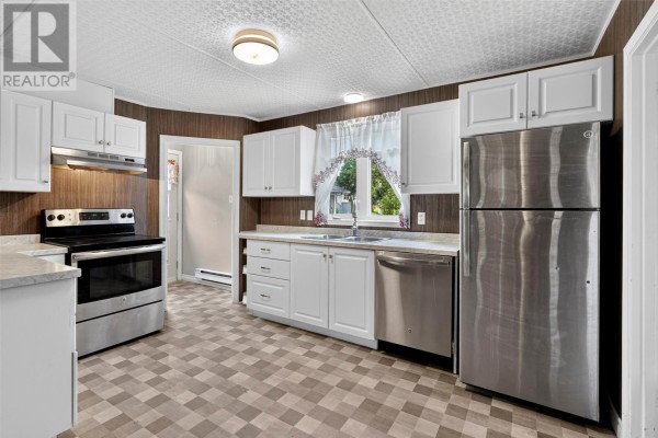 A kitchen with white cabinets, stainless steel appliances, a dark wood-paneled accent wall, and a checkered floor. - 253 Water Street, Bay Roberts