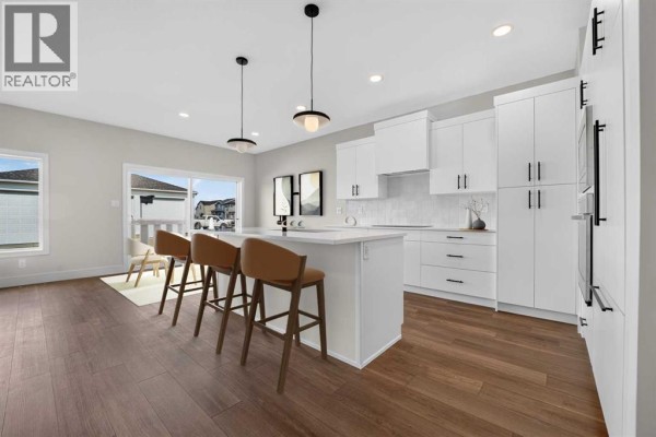 Modern kitchen with white cabinets, a white island with three bar stools, and dark wood flooring. - 2530 44 Street S, Lethbridge