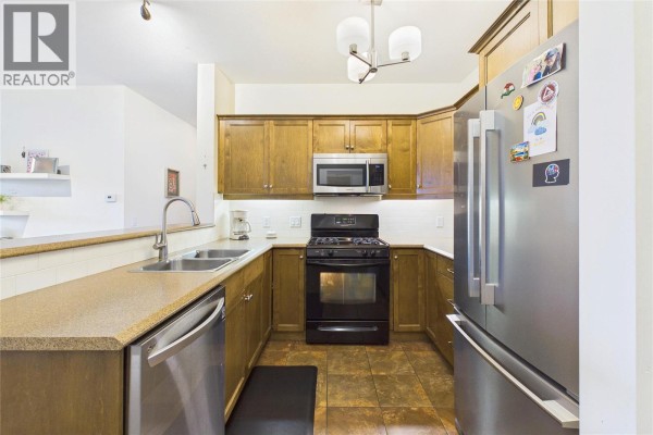 U-shaped kitchen with wooden cabinets, granite countertops, stainless steel appliances, and tiled floor. - 2532 Shoreline Drive Unit# 317, Lake Country