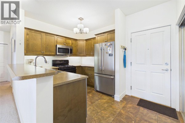 Kitchen with wooden cabinets, stainless steel appliances, tiled floor, and view of front door. - 2532 Shoreline Drive Unit# 317, Lake Country