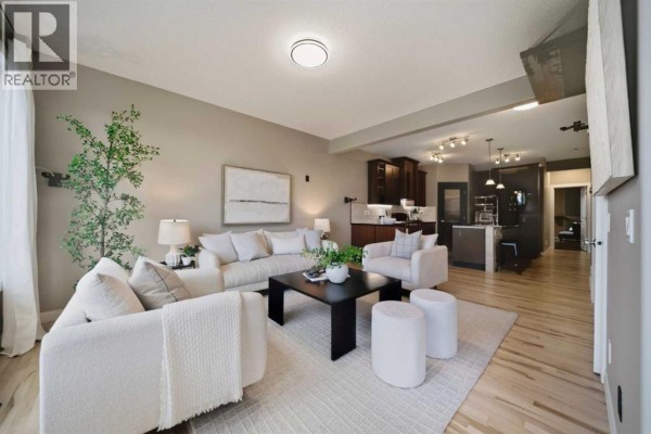 Living room with a large sectional sofa, accent chairs, a coffee table, and a view of the kitchen. - 2534 Ravenswood View Se, Airdrie