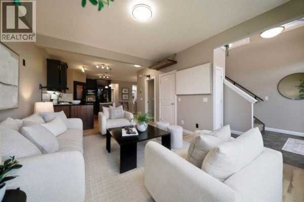 Living room with cream sofas, a black coffee table, and a view of the kitchen and staircase. - 2534 Ravenswood View Se, Airdrie