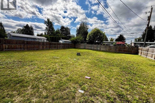 View of a large, fenced backyard with green grass and a wooden fence under a cloudy sky. - 2535 Hammond Avenue, Prince George