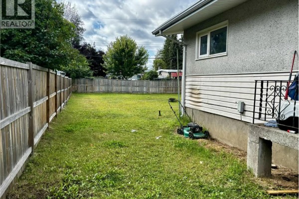 Side view of a house with a lawn, lawnmower, and a wooden fence surrounding the backyard. - 2535 Hammond Avenue, Prince George
