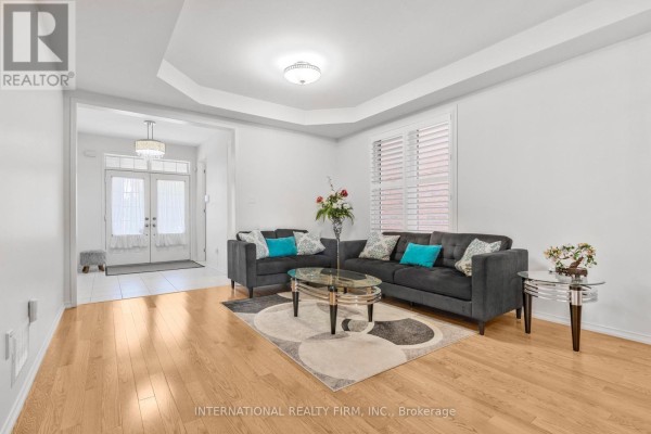 Living room with a dark grey sofa, blue accent pillows, and hardwood floors. - 2537 Snow Knight Drive, Oshawa