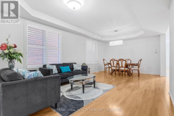 Living and dining area with a grey sofa, wooden dining table, and hardwood floors. - 2537 Snow Knight Drive, Oshawa