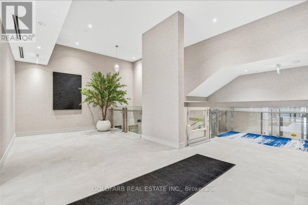 Interior view of a building lobby with a decorative tree, elevator, and a modern abstract painting. - 254 - 333 Sunseeker Avenue, Innisfil