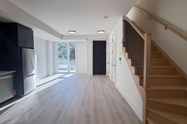 View from kitchen showing glass doors leading outside, a black door, and a wooden staircase with metal spindles. - 254 Ellis Avenue, St  Catharines