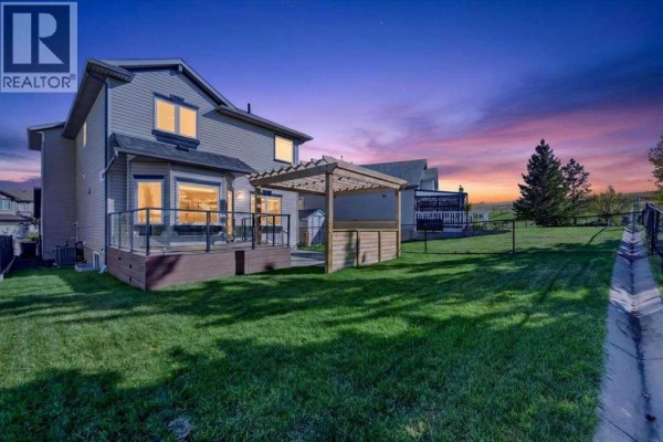 Backyard with a wooden deck, pergola, and fenced grass area at dusk. - 254 Panamount Close Nw, Calgary