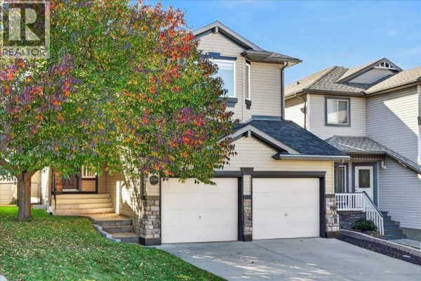 Front exterior of a two-story beige home with a double garage and mature tree. - 254 Panamount Close Nw, Calgary