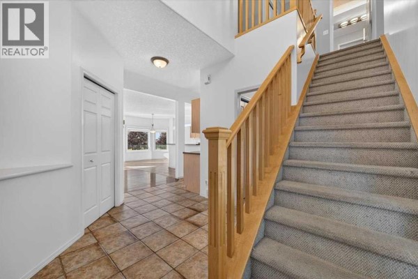 Interior foyer with beige tiled floor and a light beige carpeted staircase. - 254 Panamount Close Nw, Calgary