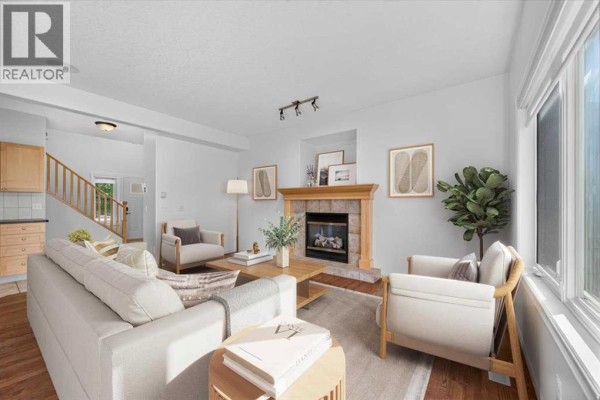 Living room with a fireplace, white sofa, two armchairs, and a wooden mantel. - 254 Panamount Close Nw, Calgary