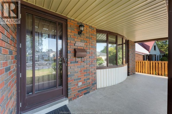 Close-up of the covered front porch entrance with brick siding, glass door, and large bay window. - 2545 St. Patricks's Avenue, Windsor