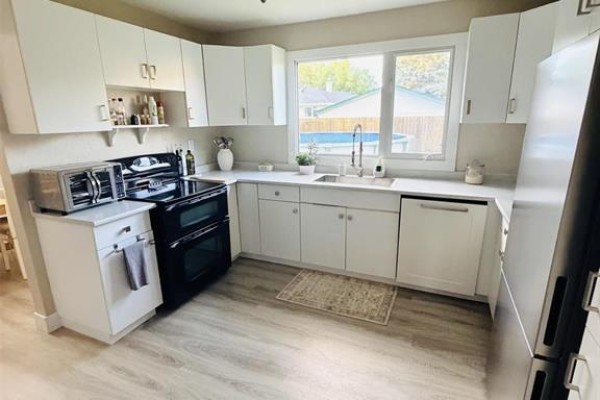 White kitchen with stainless steel appliances, a black stove, and light gray flooring. - 255 Antrim Road, Winnipeg