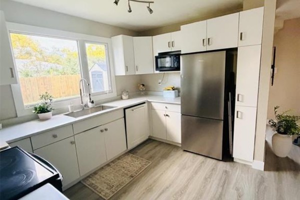 White kitchen with stainless steel refrigerator, microwave, white cabinets, and light gray flooring. - 255 Antrim Road, Winnipeg