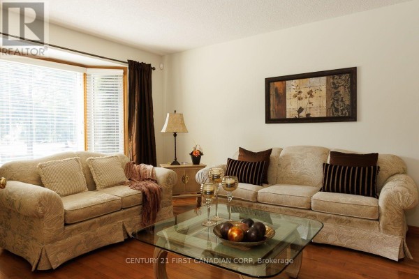 Living room with hardwood floors, beige sofas, a glass coffee table, and a bay window. - 255 Deveron Crescent, London South