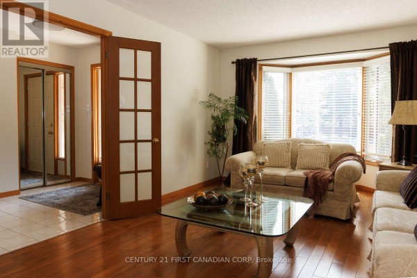 Living room with two sofas, a glass coffee table with decorative items, and a large bay window. - 255 Deveron Crescent, London South