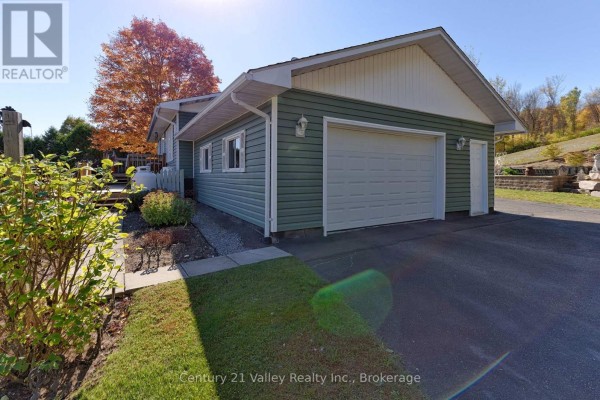 Side view of the house with garage, landscaped garden, and autumn trees. - 255 Flat Road, Greater Madawaska