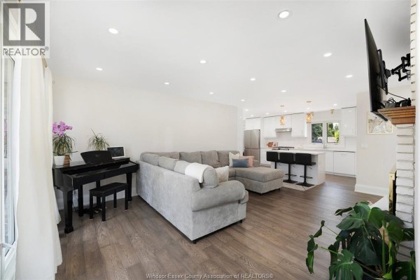 Modern white kitchen with island, bar stools, stainless steel appliances, and pendant lights. - 255 Fort Street, Amherstburg