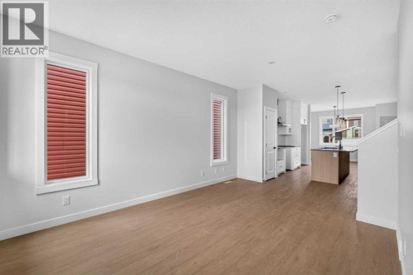 Living room showing light wood flooring, large windows, and open doorway to the kitchen. - 255 Lucas Gate Nw, Calgary