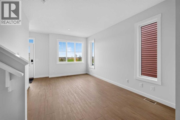 Empty room with light wood flooring, large windows, and a view of the outdoors. - 255 Lucas Gate Nw, Calgary