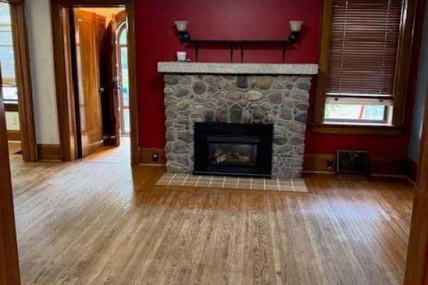 Living room with a stone fireplace, red walls, and hardwood floors. - 255 Main Street, Cambridge