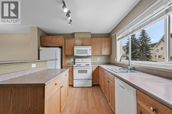 Kitchen with light wood cabinets, white appliances, and a large window. - 255 Prestwick Acres Lane Se, Calgary