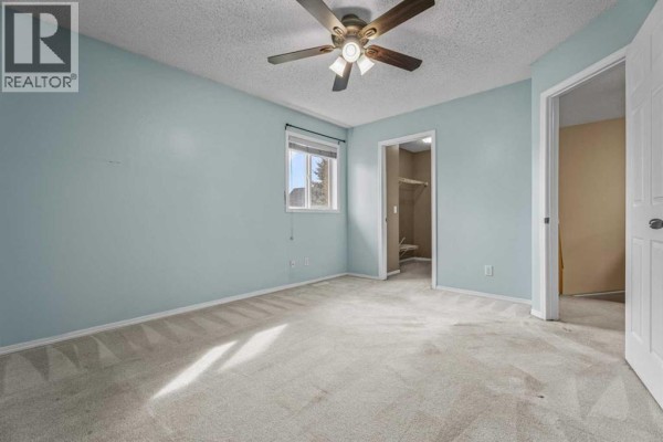 Primary bedroom with light blue walls, carpeted floor, and a ceiling fan. - 255 Prestwick Acres Lane Se, Calgary