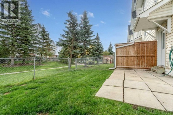 Backyard patio with a grassy lawn and a wooden fence, bordered by trees. - 255 Prestwick Acres Lane Se, Calgary