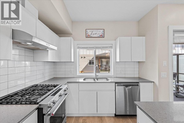 U-shaped white kitchen with stainless steel range, dishwasher, white subway tile backsplash, and window. - 255 Taylor Road Unit# 17, Kelowna