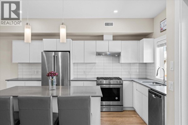 White kitchen with a large island, stainless steel refrigerator, range, and white cabinetry. - 255 Taylor Road Unit# 17, Kelowna