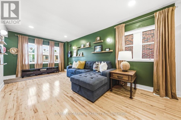 Living room with a large sectional sofa, light wood floors, green walls, and gold curtains. - 255 Weir Street N, Hamilton
